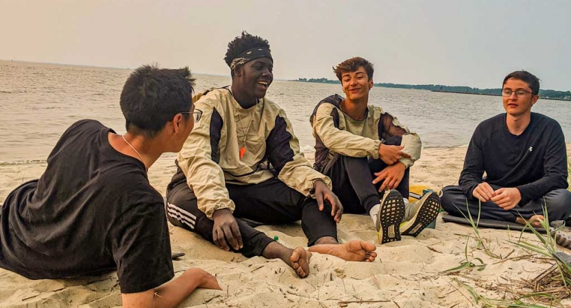 a group of teens sit on a beach while on a kayaking course